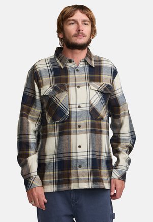 Cămașa din flanel în nuanțe de crem, albastru marin și maroniu, cu un model în carouri. Dispune de două buzunare pe piept, închideri cu butoni și un guler clasic. Textură moale.