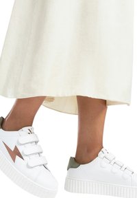 Baskets blanches avec une semelle texturée et des bandes Velcro, mettant en avant un accent en éclair rose doré et un onglet de talon vert.