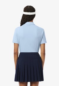 Camisa polo azul clara con cuello, combinada con una falda plisada azul marino. El conjunto cuenta con mangas cortas y una textura suave.