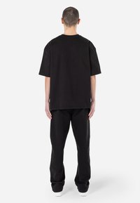 Czarna bawełniana koszulka oversized z krótkimi rękawami, okrągłym dekoltem i luźnym krojem, połączona z czarnymi zwężanymi spodniami dresowymi. Prosty design, bez wzorów.