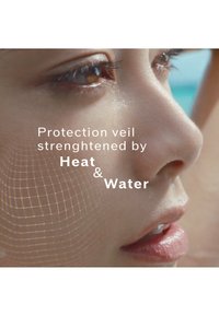 Gros plan sur un visage avec une peau lisse, des yeux bruns et un léger éclat. Des superpositions de texte mettent en évidence un voile protecteur renforcé par la chaleur et l'eau.