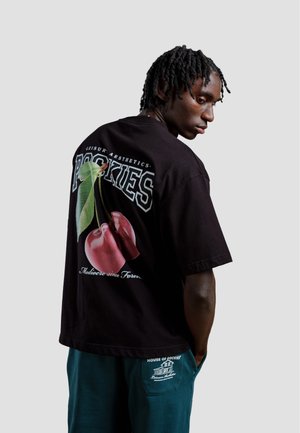 Zwarte katoenen t-shirt met een grote grafische afbeelding van kersen en bladeren op de achterkant, met vet witte letters en een ontspannen pasvorm.