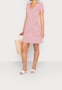 Rood en wit bloemenpatroon kortmouwig jurkje met een V-hals, uitlopende zoom en een gestructureerde afwerking. Gecombineerd met een geweven mandtas en witte slide-schoenen.