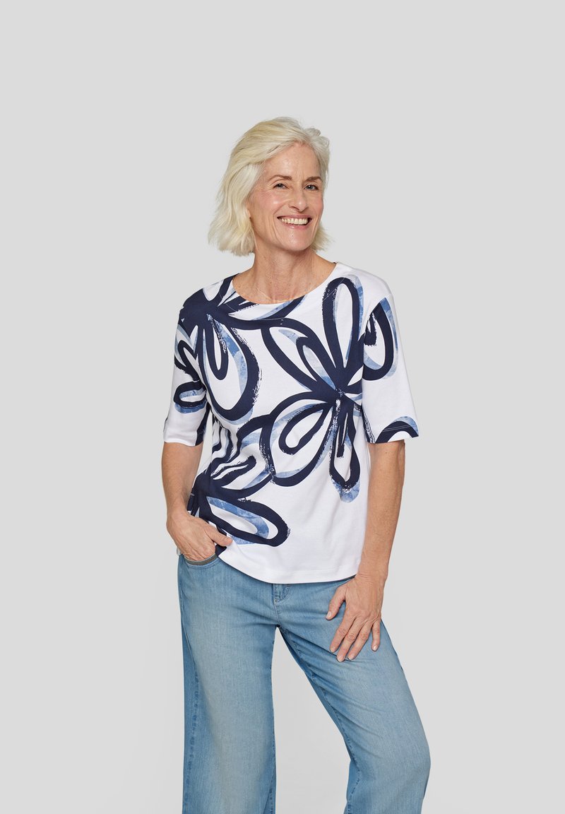 White t-shirt with navy blue floral design, round neckline, and elbow-length sleeves, paired with light blue wide-leg jeans.
