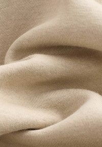 Tela de algodón beige con una textura suave y lisa y un sutil patrón acanalado, mostrando pliegues y arrugas delicados.