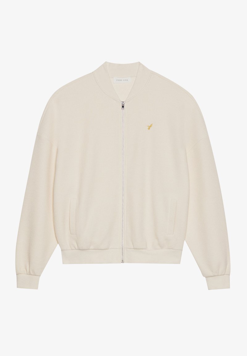 Weißer Zip-Up Hoodie mit gerippter Textur, gerippten Bündchen und Saum, Seitentaschen und einem kleinen goldenen Logoakzent auf der Brust.