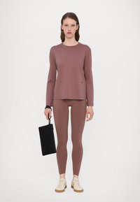 Mauvas krāsas garām piedurknēm topiņš saskaņots ar mauvas krāsas legingiem. Apģērbs izceļas ar mīkstu, elastīgu audumu. Melns clutch somiņa, kuru tur ar cilpu veidotu rokturi.