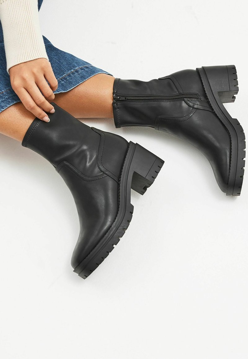 Svarta läderankelbooties med en åtsittande skaft, bred klack, ribbade sulor och sidodetalj med dragkedja. Slät textur med rundade sömsdetaljer.