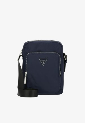 Bolso bandolera compacto azul marino con bolsillo frontal con cremallera, logo plateado de GUESS y correa negra ajustable.