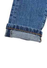 Denimin farkkushousujen hem osa taitetulla lahkeella, jossa on tummansininen väri. Sisäpuolella näkyy vaaleansininen raidallinen kuvio. Näkyvät ompeluyksityiskohdat.