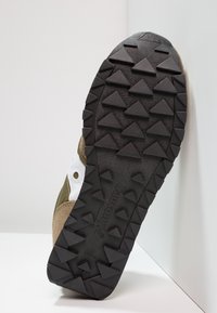 Sole boty s černou gumovou základnou, která má drsný dezén z trojúhelníkových tvarů, a hnědým semišovým postranním akcentem s bílými detaily.