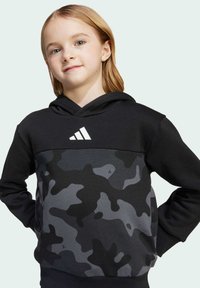 Czarna bluza z kapturem z szarym wzorem w kamuflaż, z białym logo Adidasa. Wykonana z miękkiego materiału, ma luźny krój i przednią kieszeń.