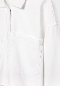 Witte denimjas met een grote voorzak en zichtbare stiksels op de schouder en kraag.