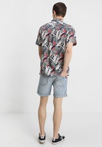 Camisa de manga corta con un colorido patrón floral en tonos de verde, rojo y beige; combinada con pantalones cortos de mezclilla enrollados y zapatillas negras.