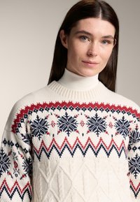 Elefántcsontszínű kötött pulóver piros és tengerészkék geometriai mintákkal, hópelyhekkel és cikkcakk mintákkal; bordázott környak-kivágással; fonott kötésű textúrával.