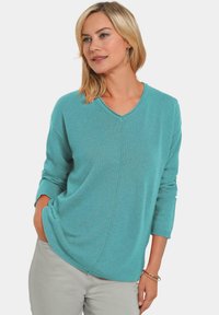 Türkiser Strickpullover mit V-Ausschnitt, langen Ärmeln und einem lockeren Schnitt. Besitzt eine dezente Rippstruktur und diagonale Nahtdetails.