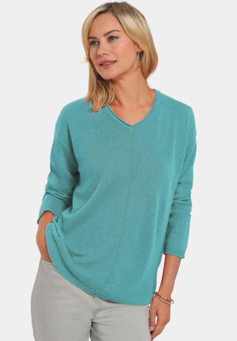 Türkiser Strickpullover mit V-Ausschnitt, langen Ärmeln und einem lockeren Schnitt. Besitzt eine dezente Rippstruktur und diagonale Nahtdetails.