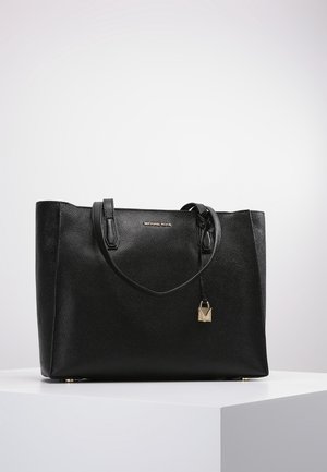 Sort læder Michael Kors tote taske med dobbelte håndtag og en lille guldlåse charm, vist på en hvid piedestal.