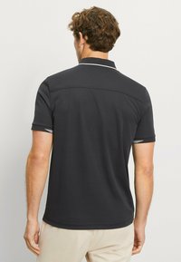 Schwarzes Poloshirt mit kurzen Ärmeln und strukturiertem Kragen. Mit weißer Borte am Kragen und an den Ärmeln. Glatte Stofftextur.