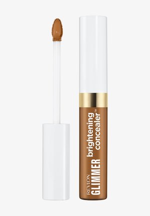 Correcteur illuminateur Revlon GLIMMER en brun moyen avec un capuchon blanc et doré, présenté avec son applicateur enduit de correcteur.