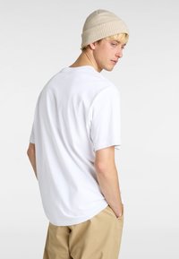 Hvid bomulds t-shirt med korte ærmer, afslappet pasform og rund hals. Båret med beige bukser og en lys farvet beanie.
