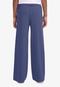 Παντελόνι με φαρδιά παντελόνα από μονόχρωμο σκούρο μπλε ύφασμα. Μαλακή υφή, ελαστική μέση και κομμένο μέχρι το πάτωμα, χωρίς ορατά σχέδια ή διακοσμητικά.