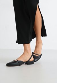Ballerines noires en cuir avec un petit talon carré, dotées d'une fine sangle sur le pied et d'un design minimaliste.