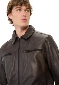 Bruine leren jas met een ritssluiting aan de voorkant, een puntige kraag en twee ritszakken op de borst. Glad textuur met een getailleerd ontwerp.