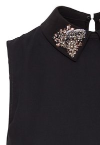 Blouse sans manches noire avec un col, ornée d'embellissements en cristal décoratifs de différentes couleurs et formes, ajoutant de la texture et du détail.