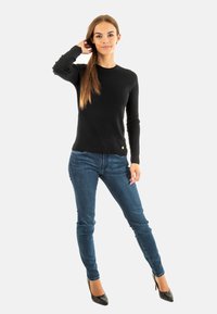 Pull noir à manches longues avec un col rond, associé à un jean bleu cintré et des escarpins noirs. Présente un petit logo en accent.