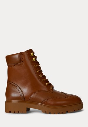 Pruunid nahast pahkluu saapad, ümmarguse toe, kuldsete silmadega ja brogue-detailidega. Paksem pruun kummitald koos tekstureeritud mustriga.