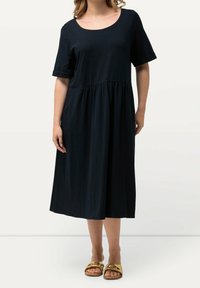 Musta puuvillamidi kleit lühikeste varrukatega ja ümaraplaaniga, kogutud talje ja voolava seeliku ning kuldsete sandaalidega.