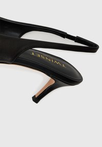 Scarpa slingback nera con tacco alto, in pelle liscia, soletta beige e tacco sottile e angolare. Presenta un design minimalista.