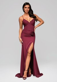 Abito da sera bordeaux con corsetto aderente, scollatura a V profonda e spalline sottili. Presenta uno spacco laterale e un accento a forma di rosa in vita. Tessuto liscio.