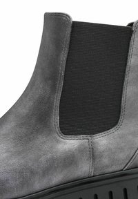 Botte Chelsea en suede gris avec panneau élastique noir sur le côté et épaisse semelle noire, montrant un gros plan de la tige et de la zone de la cheville.