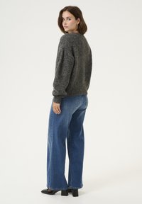 Grijze gebreide trui met drop shoulders, gecombineerd met wijde blauwe jeans. De outfit wordt compleet gemaakt met zwarte hakken. Eenvoudig ontwerp.