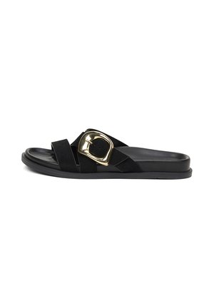 Schwarze flache Slide-Sandale mit gekreuzten Riemen und großer goldener Schnalle auf weißem Hintergrund.