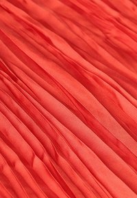 Tissu plissé rouge avec une texture lisse et des plis verticaux réguliers, créant une apparence fluide et superposée.