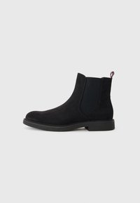 Botín Chelsea negro de ante con paneles laterales elásticos, puntera redonda, suela de goma texturizada y un pequeño tirador de detalle en rojo, blanco y azul.
