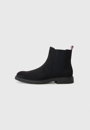 Botín Chelsea negro de ante con paneles laterales elásticos, puntera redonda, suela de goma texturizada y un pequeño tirador de detalle en rojo, blanco y azul.