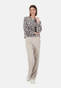 Leopardenmuster Pullover aus weichem Stoff, kombiniert mit beigen weiten Hosen und weißen Sneakers. Lässiges Design mit langen Ärmeln und Knöpfen.