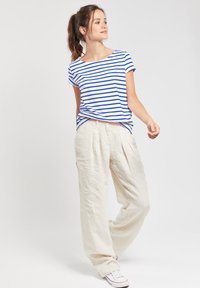 T-shirt rayé en blanc et bleu, porté avec un pantalon en lin beige ample. La tenue présente une coupe décontractée et est associée à des baskets blanches.