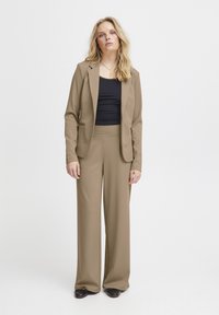 Beige räätälöity bleiseri ja leveälahkeiset housut pehmeästä kankaasta, yhdistetty mustaan toppiin. Minimalistinen muotoilu ilman näkyviä kuvioita tai koristeluja.