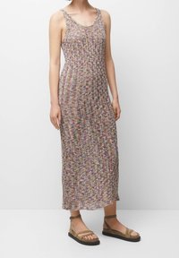 Un vestido maxi de punto multicolor con un corpiño ajustado, tirantes anchos y una falda fluida. Combinado con sandalias marrones de tiras.