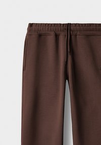 Brune joggebukser med elastisk midje, snøring og sidelommer. Glatt tekstur og smale ben. Diskret logo detalj.