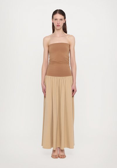 Brown strapless top paired with a beige, flowing maxi skirt. The fabric appears soft and smooth, creating a clean, streamlined silhouette.