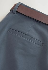 Graue Stoffhosen mit glatter Textur, versehen mit einem braunen Ledergürtel und einer Gesäßtasche mit gerader Nahtdetail.