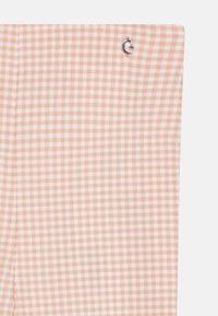 Tissu à motif vichy en pêche et blanc avec un accent logo argenté. La texture semble lisse, avec un design classique à carreaux.
