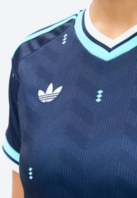 Nahaufnahme eines dunkelblauen Sportshirts mit hellblauen Akzenten, Adidas-Logo auf der Brust und dezent gemusterter Textur.