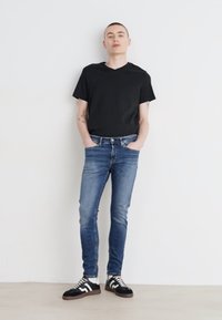 Čierne bavlnené tričko, modré denimové džínsy so slim fit, stredné opranie a tenisky s čiernymi, bielymi a šedými vzormi.